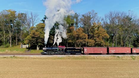 Una-Vista-Aérea-De-Un-Antiguo-Tren-De-Pasajeros-De-Carga-A-Vapor-Que-Sopla-Humo-Mientras-Viaja-Lentamente-En-Un-Día-De-Otoño