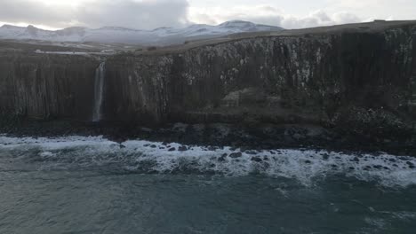 Kilt-rock-and-mealt-falls-in-scotland-with-snow-covered-hills-in-the-background,-overcast-weather,-aerial-view