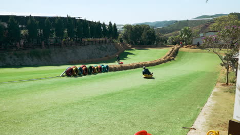 Adult-Man-Rides-Cart-from-Grassy-Hill-at-Mongo-Land-Park,-Da-Lat-Vietnam