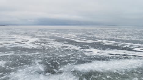 Expansive-view-of-a-frozen-lake-under-overcast-skies,-slight-snow-cover-and-ice-patterns-visible-in-Lithuania,-aerial-view