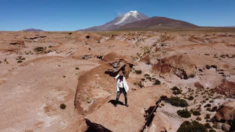 Mujer-Baila-Sobre-Un-Afloramiento-Rocoso-En-El-Altiplano-Boliviano,-Volcán-Distante