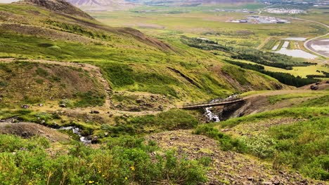 Small-wooden-hiking-trail-bridge-over-mountain-stream-in-Iceland,-panning-view