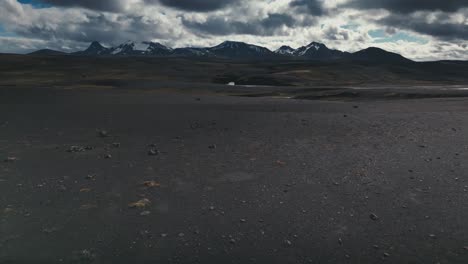 Drone-aerial-shot-that-skims-the-rocky-terrain-and-tilts-up-to-reveal-a-gorgeous-snow-capped-mountain-range