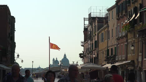 Se-Desarrollan-Escenas-A-Lo-Largo-De-Las-Calles-De-Venecia,-Repletas-De-Turistas,-Con-El-Telón-De-Fondo-De-La-Bandera-Veneciana,-San