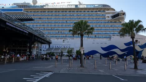 Cruise-ship-docked-at-Sydney-port-with-passengers-milling-about,-sunny-day-backlit