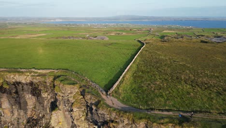 Cliffs-of-moher-in-ireland,-green-landscape,-ocean-backdrop,-sunny-day,-aerial-view