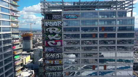 Aerial-rising-shot-around-a-skyscraper-covered-in-Graffiti,-in-sunny-Los-Angeles