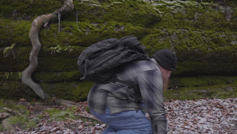 slow-motion-shot-of-a-hiker-jumping-down-from-a-boulder-onto-the-leaf-covered-forest-floor-and-continuing-along-the-moss-covered-cliff-of-the-ledges