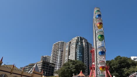 Colorful-Ferris-wheel-spins-in-Sydney-against-a-clear-sky,-urban-backdrop,-daytime