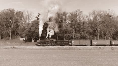 An-Aerial-View,-in-Black-and-White,-of-an-Antique-Steam-Freight-Passenger-Train-Blowing-Smoke-as-it-Slowly-Travels-on-an-Autumn-Day