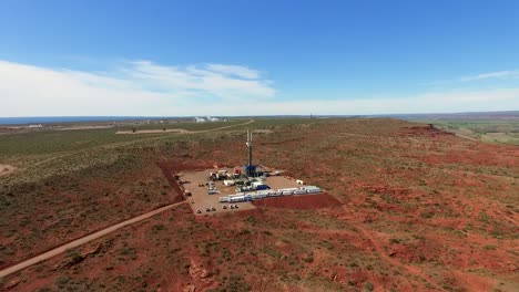 Oil-drill-rig-in-vast-red-desert,-industry-amidst-nature,-daytime,-aerial-view