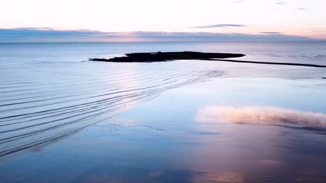 Picturesque-drone-shot-of-the-calm-ocean-waves-rolling-up-the-sand-on-Skerries-Beach-during-sunrise,-Republic-of-Ireland