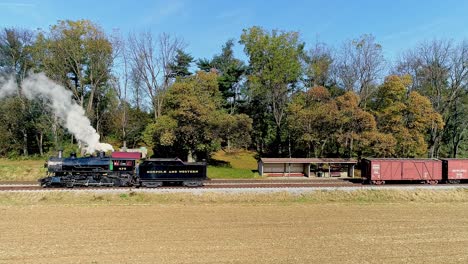 An-Aerial-View,-of-an-Antique-Steam-Freight-Passenger-Train-Blowing-Smoke-as-it-Slowly-Travels-on-an-Autumn-Day