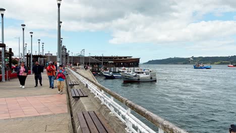 Gente-Caminando-Por-El-Paseo-Marítimo-Dalcahue,-Mercado-De-Artesanía-Tradicional-Junto-Al-Puerto,-Isla-De-Chiloé.