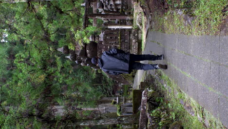 Un-Turista-Masculino-Solitario-Con-Impermeable-Caminando-Explorando-El-Cementerio-De-Okunoin-En-Koyasan-Por-Su-Cuenta