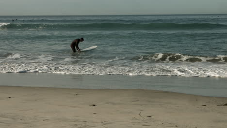 A-middle-aged-surfer-heads-into-the-ocean-at-a-beach-in-Cardiff-California