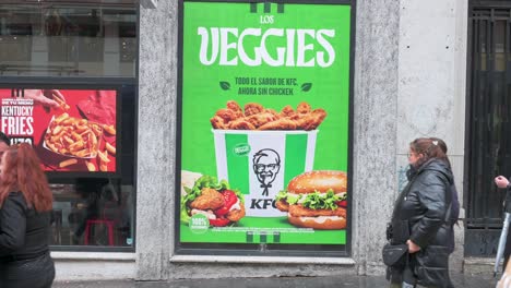 Los-Peatones-Pasan-Junto-A-Un-Anuncio-Comercial-De-KFC-En-La-Calle-Que-Muestra-Una-Nueva-Comida-Vegetariana-Llamada-Verduras-Disponible-En-Sus-Cadenas-De-Comida-Rápida-En-España.