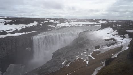 Majestätischer-Wasserfall,-Der-über-Eine-Klippe-In-Island-Stürzt,-Umgeben-Von-Schnee-Und-Einzigartigen-Landschaftsmustern