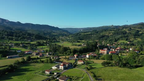 descent-flight-with-a-drone-in-a-rural-area-with-rustic-houses-spread-between-cultivated-meadows,-livestock-areas-and-oak-forests-with-mountains-in-the-background-in-a-Cantabra-Basque-village,-Spain