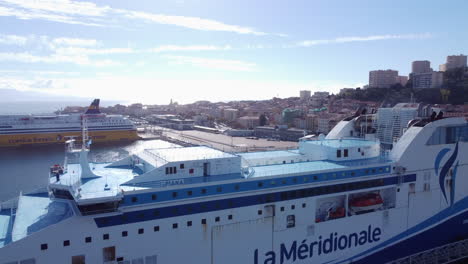 Aerial-flying-backwards-from-Ajaccio-on-sunny-day,-revealing-cruise-ship-docked