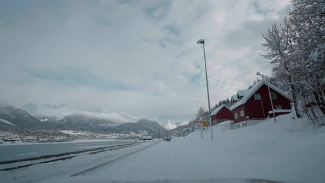 POV-video-of-a-daytime-drive-through-the-snowy-roads-of-Norway's-Western-Fjords,-surrounded-by-tall,-snow-covered-mountains-with-trees