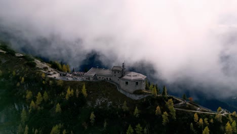 Aerial-view-of-a-majestic-stone-castle-perched-atop-a-mountain-peak,-shrouded-in-mist