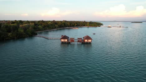 Long-Wooden-Pier-Leading-to-Two-Over-Water-Bungalows-Resort-At-Sunset-at-Leebong-Island,-Belitung-Indonesia---Aerial-Parallax