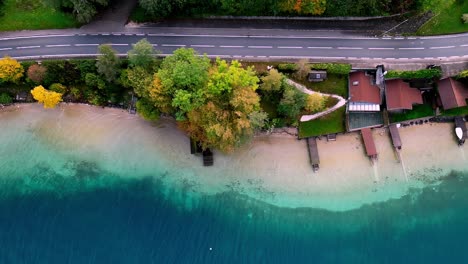 Der-Ruhige-See-Spiegelt-Das-Leuchtende-Herbstlaub-Wider,-Segelboote-Ruhen-Auf-Dem-Glasklaren-Wasser,-In-Der-Ferne-Erheben-Sich-Berge