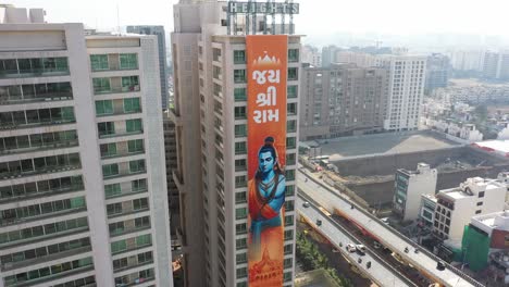 Vista-Aérea-De-Drones-De-Rajkot,-Hay-Muchos-Edificios-Debajo-Y-Arriba-Y-El-Estandarte-De-Jai-Shri-Ram-Es-Visible-En-El-Gran-Edificio-De-Rajkot.