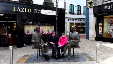 Lovely-old-couple-sitting-in-a-bench-between-Oscar-Wilde-and-Eduard-Vilde-statues,-Galway