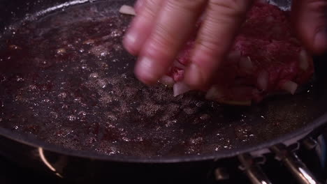 Caucasian-man-uses-hand-to-flatten-hamburger-cooking-in-hot-skillet