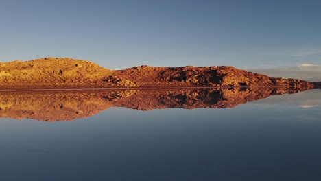 Golden-altiplano-rock-landscape-reflected-in-Uyuni-salt-lake,-Bolivia