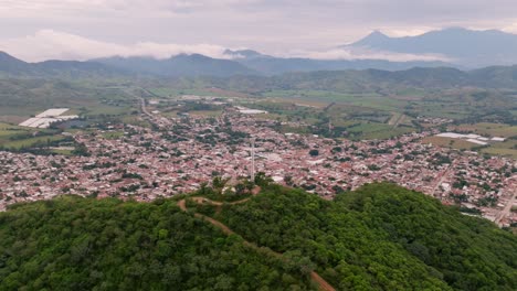 Tecalitlan-Hill-of-the-Cross:-aerial-panorama-of-peaks,-valley-and-Colima-volcano-amidst-a-cloudy-blue-sky