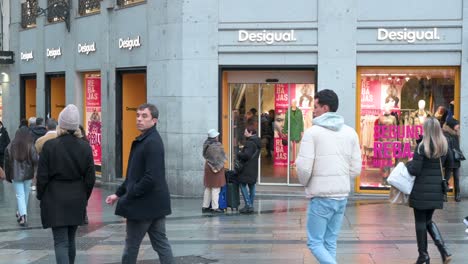 On-a-bustling-commercial-street,-pedestrians-walk-past-the-Spanish-clothing-brand-Desigual-store-in-Spain