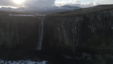 Majestic-Kilt-Rock-Waterfall-in-Skye,-Scotland,-with-snow-capped-mountains-in-the-background-at-dusk