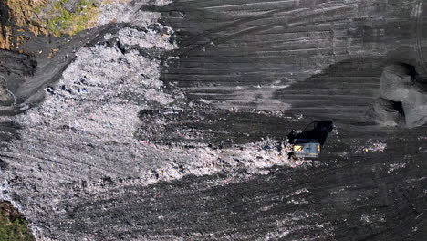 Top-down-static-aerial-footage-of-a-bulldozer-pushing-trash-around-in-a-landfill