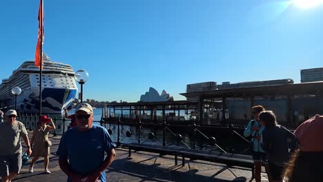 Bright-sunny-day-at-Sydney-Harbour-with-tourists-and-a-cruise-ship,-Sydney-Opera-House-in-the-background,-clear-blue-sky