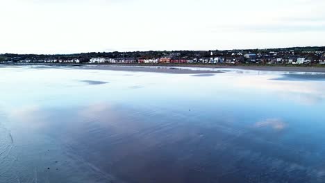 Disparo-Aéreo-De-Un-Dron-Pasando-Sobre-Las-Tranquilas-Aguas-Reflectantes-Del-Mar-De-Irlanda-En-Dirección-A-La-Playa-De-Skerries,-Irlanda