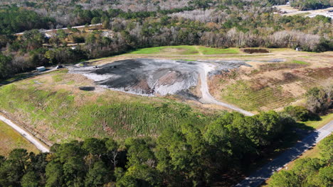 Wide-aerial-flyover-of-a-landfill-that-has-not-seen-much-use-in-southern-Georgia-with-a-small-bulldozer-moving-trash-around