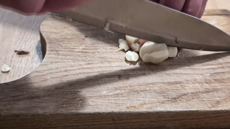 Close-up-shot-of-hand-cutting-ginger-into-pieces-on-a-wooden-board-on-the-table-inside-a-kitchen