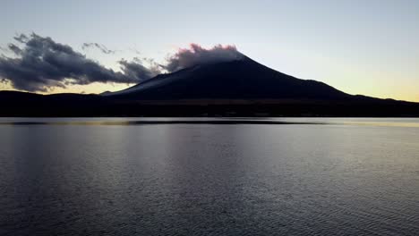 Dawn-breaks-over-a-tranquil-lake-with-a-majestic-mountain-backdrop,-clouds-gently-caressing-its-peak