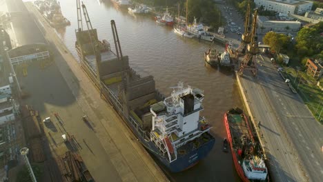 A-busy-port-at-sunrise-with-ships-and-cranes,-warm-golden-light,-aerial-view