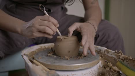 Potter-carefully-uses-cutting-ribbon-tool-to-refine-clay-pot-on-rotating-wheel-MEDIUM-SHOT