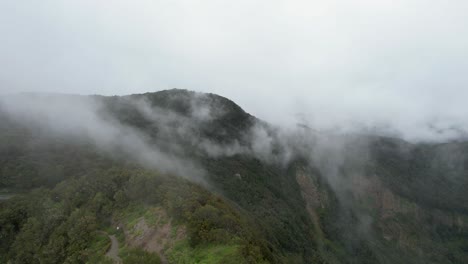 Birds'-eye-view-of-a-trail-revealing-tall,-green-mountain-peaks,-with-clouds-swirling-around,-La-Gomera-Island