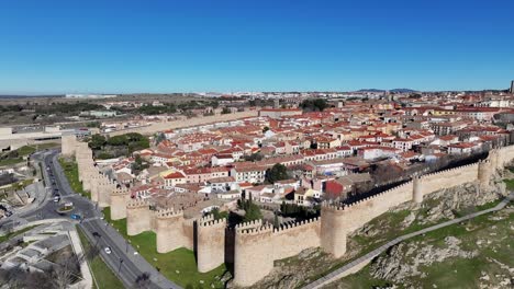 Orvita-flight-over-the-Unesco-World-Heritage-city-seeing-its-southern-walls-and-its-road-with-cars-circulating-and-its-internal-homes-on-a-winter-day-with-a-blue-sky-in-Avila-Spain