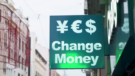 A-green-sign-from-a-currency-exchange-business-displays-the-words-'Change-Money'-alongside-symbols-representing-various-available-currencies-such-as-Japanese-yen,-US-dollar,-and-euro