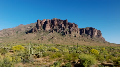 Dry-green-arid-scrubland-cactus-and-shrubs-sit-below-Superstition-Mountains-against-blue-sky-in-Arizona