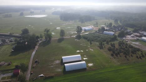 Sunny-morning-over-white-arched-hall-in-field-steam-atmosphere-aerial