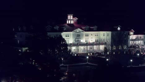 Aerial-orbit-left-to-right-behind-trees-establishes-front-courtyard-of-hotel-at-night-illuminated-by-lighting