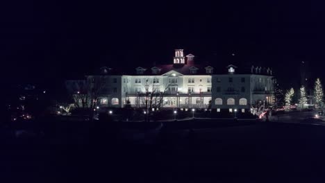 Right-to-left-pan-across-courtyard-to-showcase-large-white-building-with-grand-arch-and-entrance-at-night